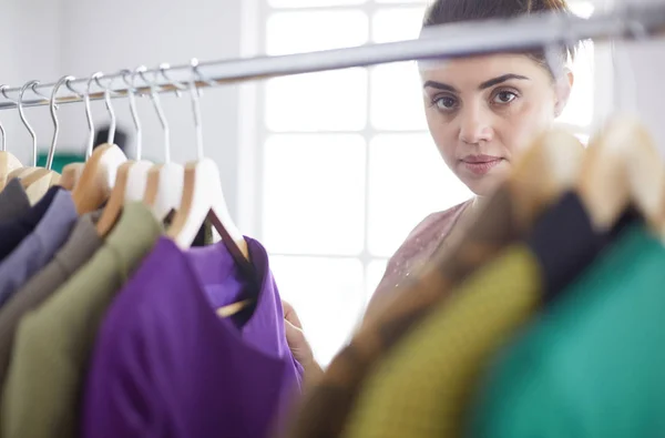 Beautiful young stylist near rack with hangers