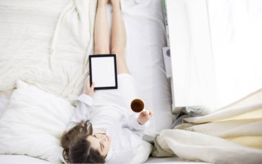 Sabahları yatakta otururken tablet kullanan ve kahve içen kadın portresi