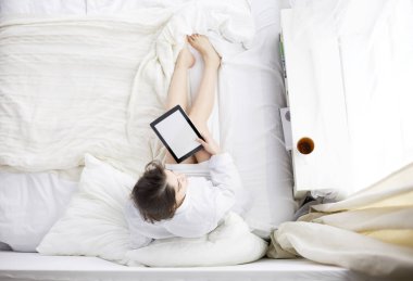 Sabahları yatakta otururken tablet kullanan ve kahve içen kadın portresi