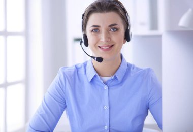 Ofisinde kulaklık takmış, telefon operatörü olarak çalışan ciddi ve güzel bir genç kadın.