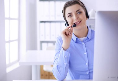 Ofisinde kulaklık takmış, telefon operatörü olarak çalışan ciddi ve güzel bir genç kadın.