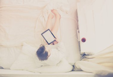 Sabahları yatakta otururken tablet kullanan ve kahve içen kadın portresi