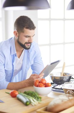 Dijital tablet ve yemek pişirme tarifine uyan bir adam evdeki mutfakta lezzetli ve sağlıklı yemekler pişiriyor.