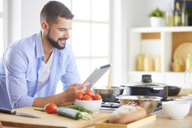 Dijital tablet ve yemek pişirme tarifine uyan bir adam evdeki mutfakta lezzetli ve sağlıklı yemekler pişiriyor.