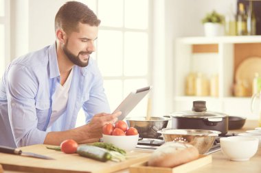 Dijital tablet ve yemek pişirme tarifine uyan bir adam evdeki mutfakta lezzetli ve sağlıklı yemekler pişiriyor.
