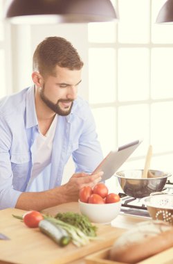 Dijital tablet ve yemek pişirme tarifine uyan bir adam evdeki mutfakta lezzetli ve sağlıklı yemekler pişiriyor.