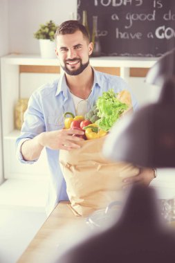 Mutfak arka planında poşet dolusu erzak tutan adam. Alışveriş ve sağlıklı gıda konsepti