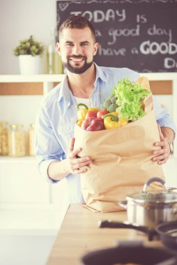Mutfak arka planında poşet dolusu erzak tutan adam. Alışveriş ve sağlıklı gıda konsepti