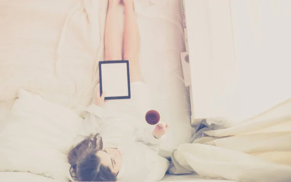 Porträtt av kvinna som använder tabletter och dricker kaffe när hon sitter på sängen på morgonen — Stockfoto