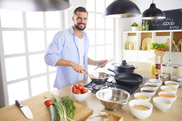 Man following recipe on digital tablet and cooking tasty and healthy food in kitchen at home