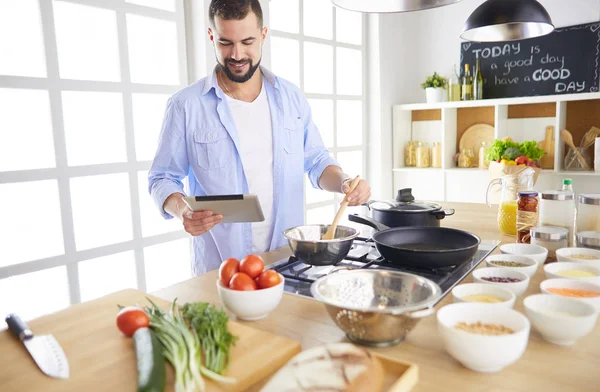 Hombre siguiendo la receta en la tableta digital y cocinar comida sabrosa y saludable en la cocina en casa — Foto de Stock