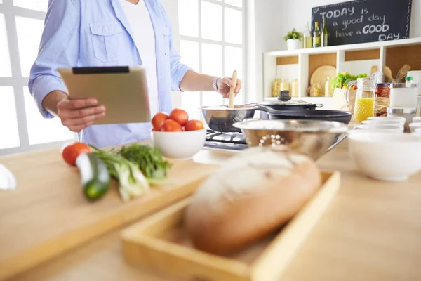 Man following recipe on digital tablet and cooking tasty and healthy food in kitchen at home — Stock Photo, Image