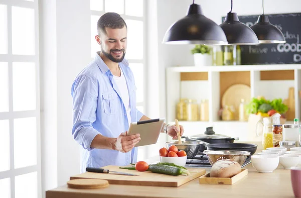 Man following recipe on digital tablet and cooking tasty and healthy food in kitchen at home