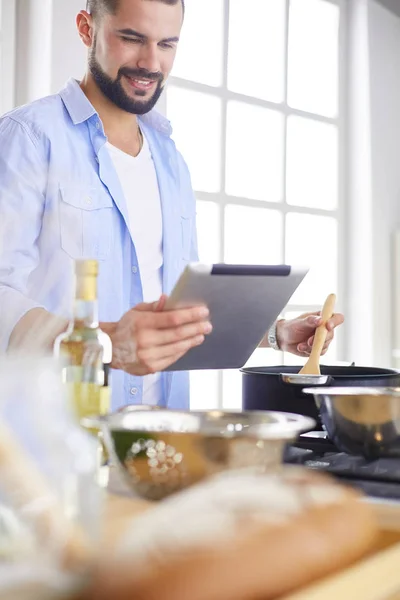 Man following recipe on digital tablet and cooking tasty and healthy food in kitchen at home
