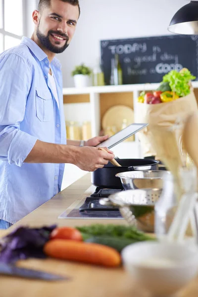 Man following recipe on digital tablet and cooking tasty and healthy food in kitchen at home — Stock Photo, Image