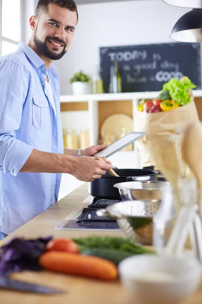 Hombre siguiendo la receta en la tableta digital y cocinar comida sabrosa y saludable en la cocina en casa — Foto de Stock