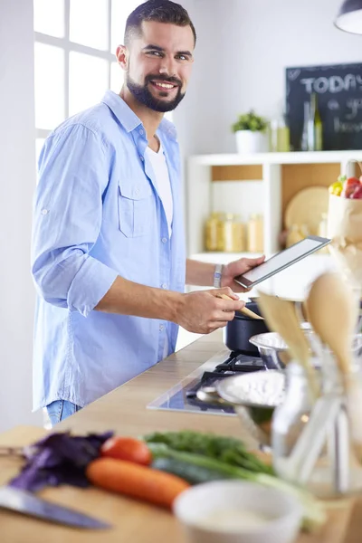 Hombre siguiendo la receta en la tableta digital y cocinar comida sabrosa y saludable en la cocina en casa — Foto de Stock