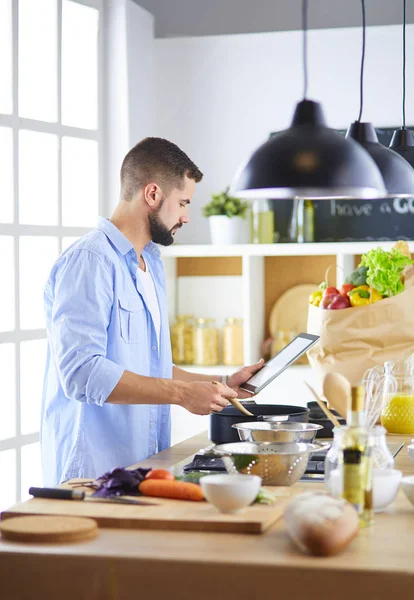 L'uomo segue la ricetta su tavoletta digitale e cucina cibo gustoso e sano in cucina a casa — Foto Stock