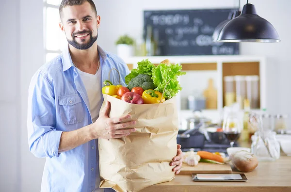 Man holding paper bag full of groceries on the kitchen background. Shopping and healthy food concept — Stock Photo, Image