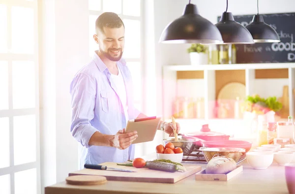 Man following recipe on digital tablet and cooking tasty and healthy food in kitchen at home