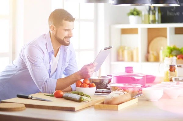 Homem seguindo receita em tablet digital e cozinhar comida saborosa e saudável na cozinha em casa — Fotografia de Stock