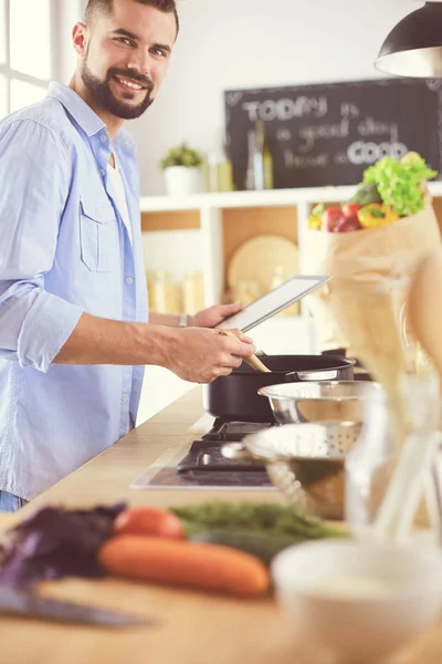 Man following recipe on digital tablet and cooking tasty and healthy food in kitchen at home