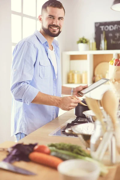 Man following recipe on digital tablet and cooking tasty and healthy food in kitchen at home — Stock Photo, Image