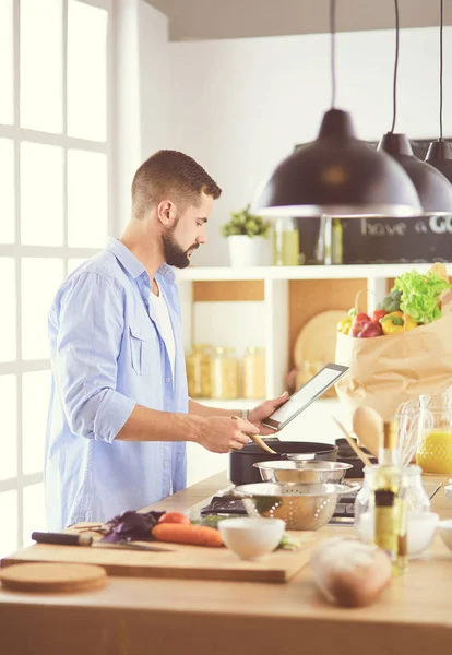 Homem seguindo receita em tablet digital e cozinhar comida saborosa e saudável na cozinha em casa — Fotografia de Stock