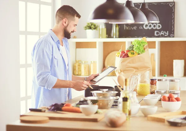 Manusia mengikuti resep pada tablet digital dan memasak makanan lezat dan sehat di dapur di rumah — Stok Foto