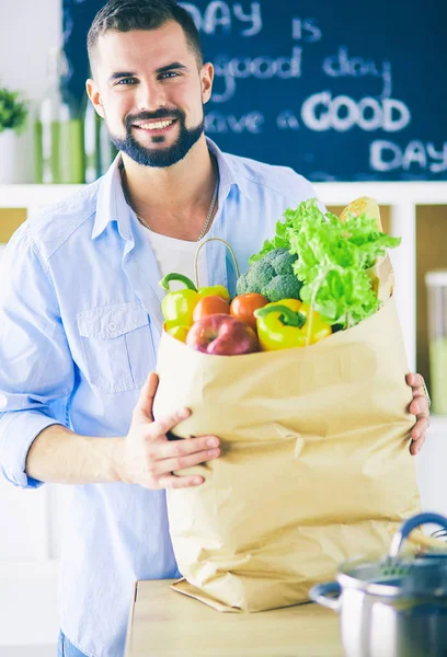 Man holding paper bag full of groceries on the kitchen background. Shopping and healthy food concept — Stock Photo, Image