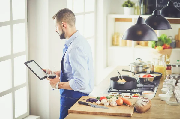 Man following recipe on digital tablet and cooking tasty and healthy food in kitchen at home