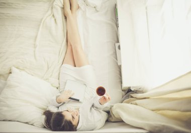 Sabahları yatakta otururken tablet kullanan ve kahve içen kadın portresi