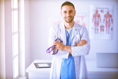 Genç ve kendinden emin erkek doktor portresi tıp ofisinde duruyor..