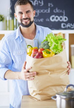 Mutfak arka planında poşet dolusu erzak tutan adam. Alışveriş ve sağlıklı gıda konsepti