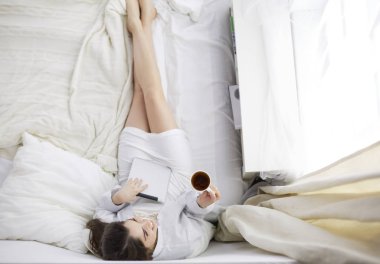 Sabahları yatakta otururken tablet kullanan ve kahve içen kadın portresi