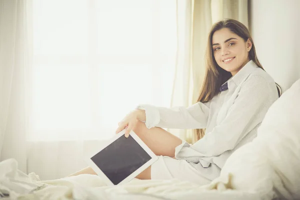 Portret van een vrouw die een tablet gebruikt en 's ochtends koffie drinkt terwijl ze op bed zit — Stockfoto