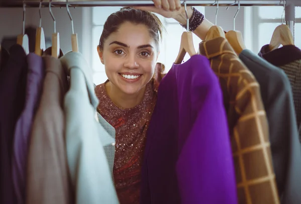 Beautiful young stylist near rack with hangers