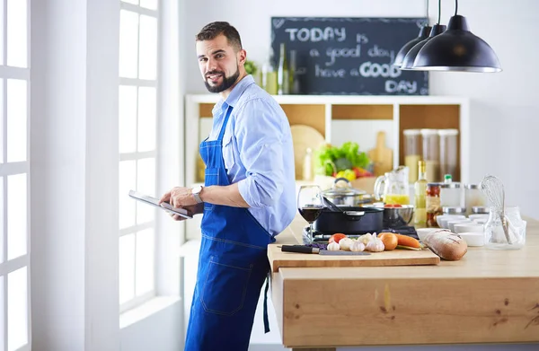 Hombre siguiendo la receta en la tableta digital y cocinar comida sabrosa y saludable en la cocina en casa —  Fotos de Stock