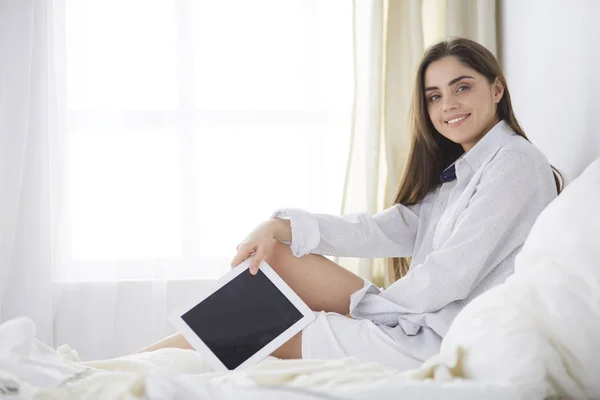 Πορτρέτο της γυναίκας χρησιμοποιώντας tablet και πίνοντας καφέ, ενώ κάθεται στο κρεβάτι το πρωί — Φωτογραφία Αρχείου