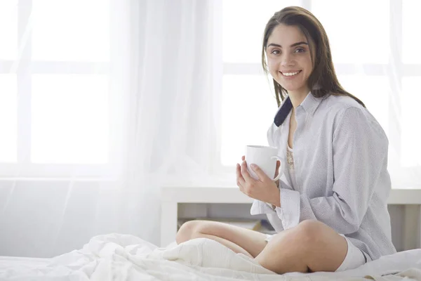 Mulher sentada na cama lendo um livro e tomando café da manhã — Fotografia de Stock