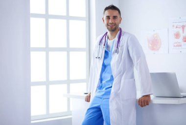 Genç ve kendinden emin erkek doktor portresi tıp ofisinde duruyor..