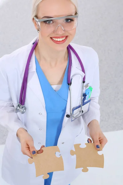 Mulher médico segurando duas peças de puzzle de conexão — Fotografia de Stock
