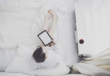 Sabahları yatakta otururken tablet kullanan ve kahve içen kadın portresi