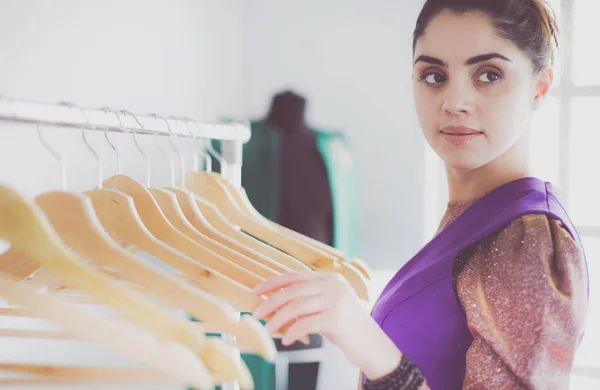 Schöne junge Stylistin in der Nähe von Gestell mit Kleiderbügeln — Stockfoto