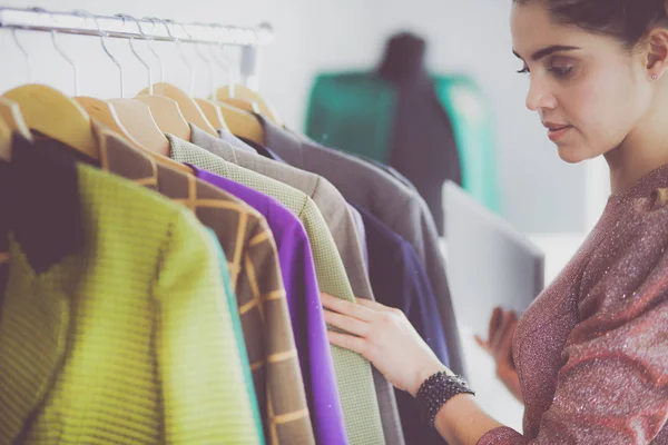 Vacker ung stylist nära rack med hängare — Stockfoto