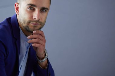 Gri arka planda yalnız oturan genç iş adamı.