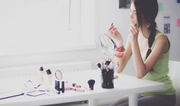 Joven hermosa mujer haciendo maquillaje cerca del espejo, sentado en el escritorio —  Fotos de Stock