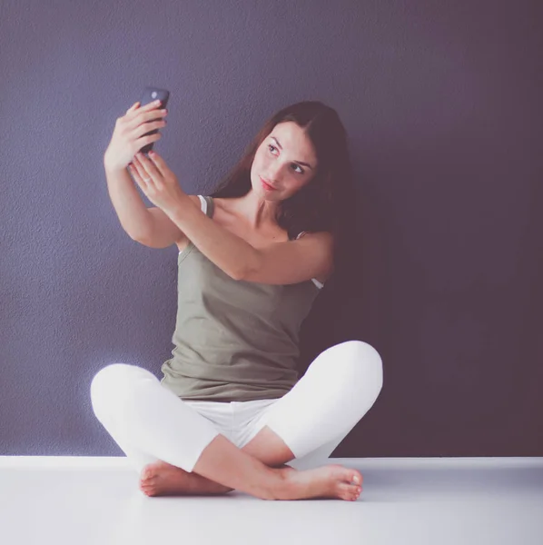 Attraente ragazza caucasica seduta sul pavimento con telefono vicino alla parete — Foto Stock