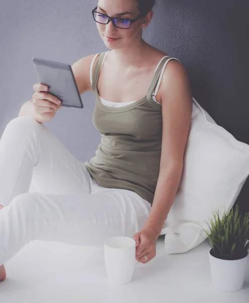 Attraente ragazza caucasica seduta sul pavimento con tazza e tablet vicino alla parete — Foto Stock