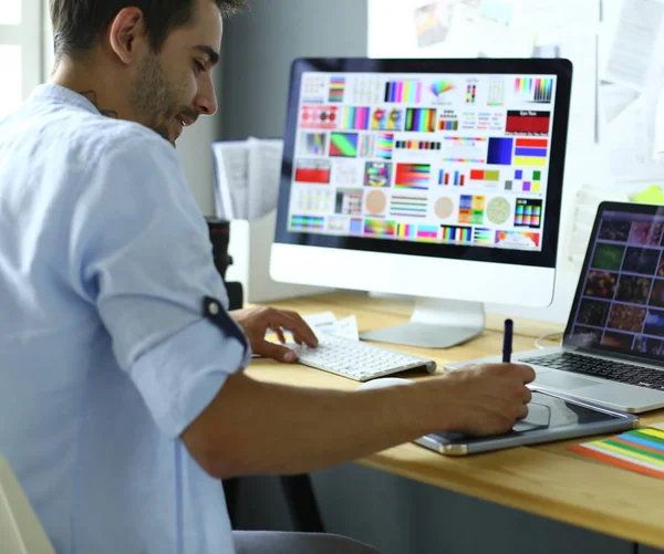 Porträt eines jungen Designers, der im Grafikstudio vor Laptop und Computer sitzt, während er online arbeitet. — Stockfoto